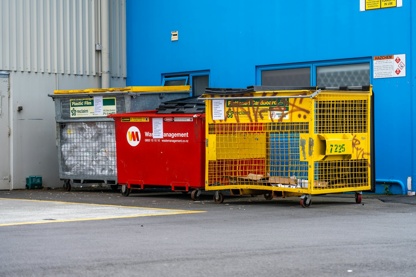 Tre cassonetti industriali allineati contro i muri di un edificio.